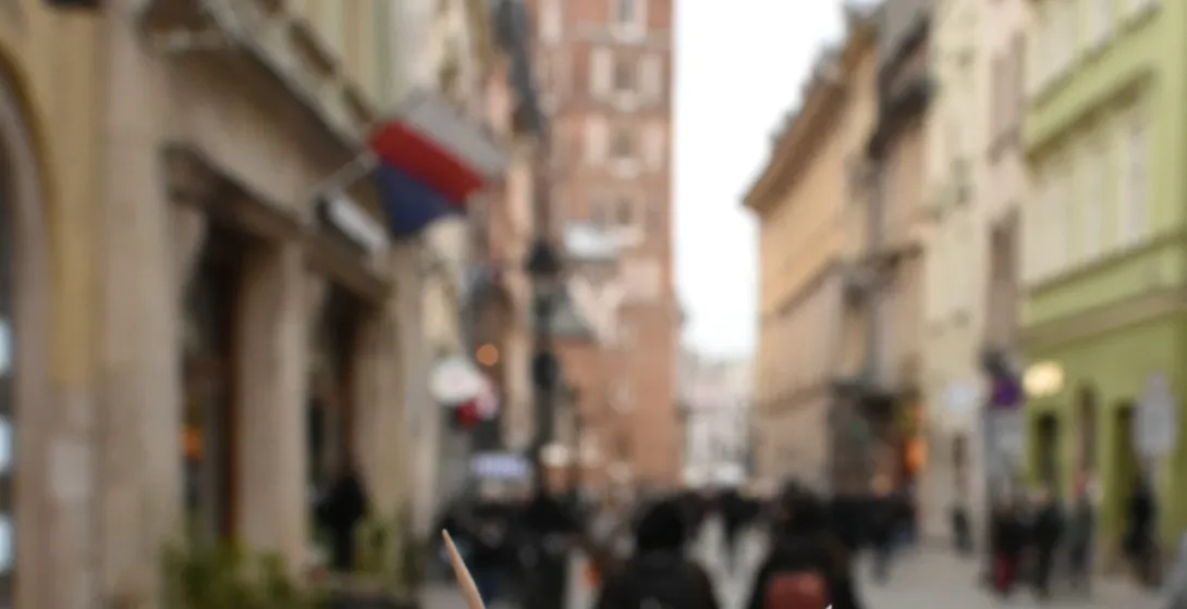 Hand holding grilled oscypek cheese with jam. St. Mary's Basilica in Kraków is blurred in the background.