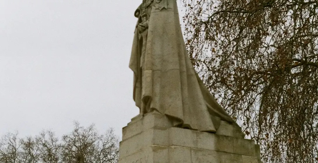 Estatua del rey Jorge V sobre un zócalo de piedra, con una paloma en la cabeza y árboles sin hojas al fondo.