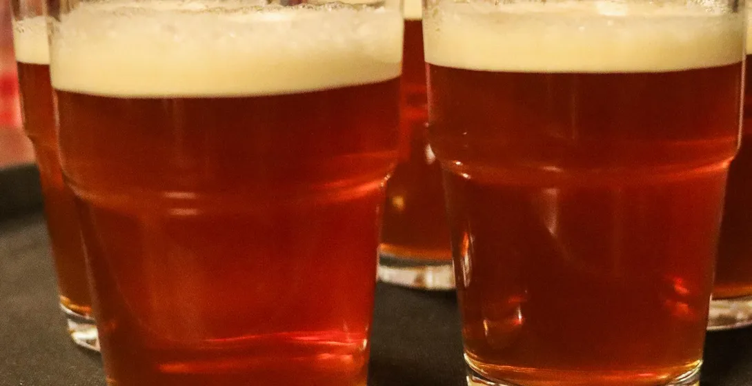 Mehrere Gläser bernsteinfarbenes Bier mit Schaumkronen stehen auf einem dunklen Serviertablett in einem Pub.