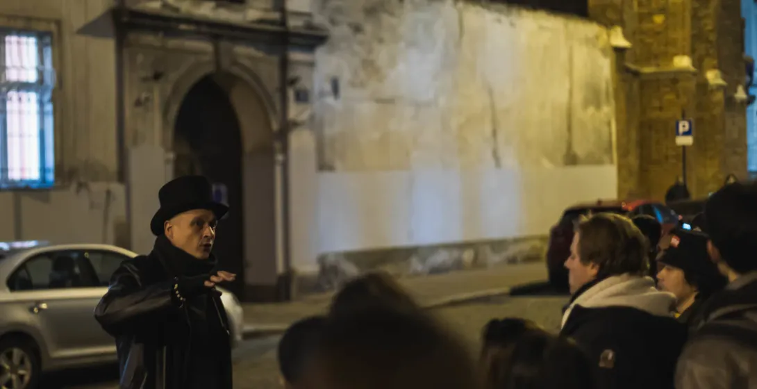 Reiseführer in Zylinder und Mantel spricht nachts mit einer Gruppe auf einer Kopfsteinpflasterstraße in Krakau. Historisch...