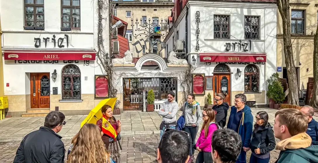 Un grupo de turistas escucha a una guía con un paraguas amarillo en la calle Szeroka del barrio de Kazimierz, Cracovia.