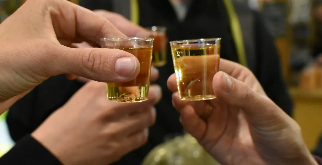 Close-up of three hands toasting with small tasting glasses of amber liquid in Krakow.