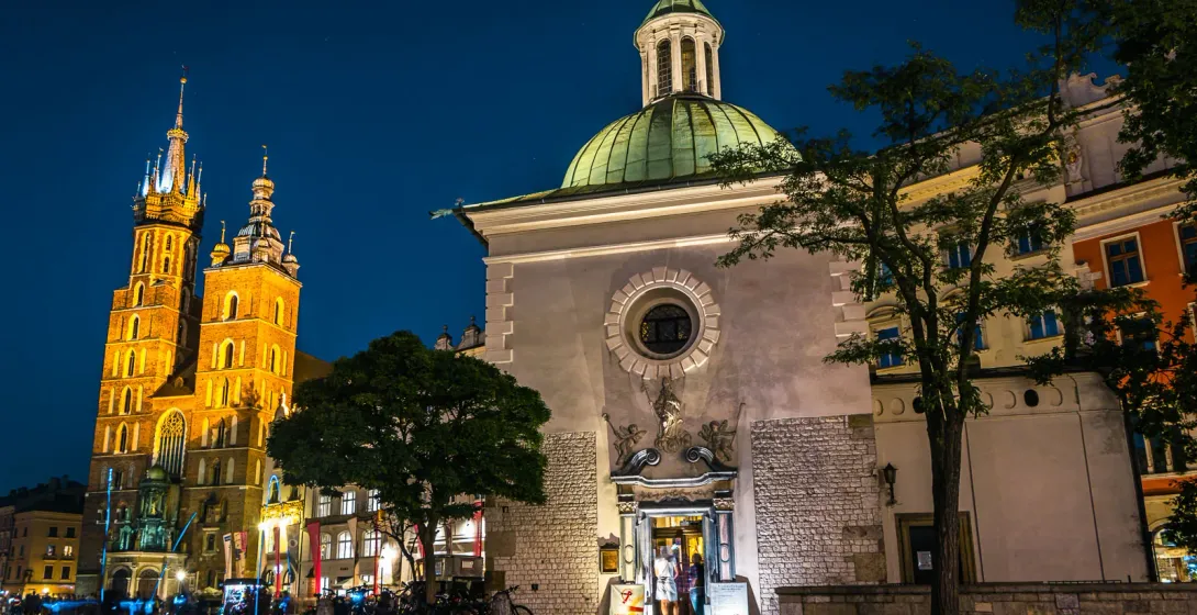 St. Mary's Basilica and St. Adalbert's Church lit up at night on Krakow's Main Market Square with wet cobblestones.