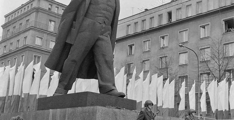 Schwarz-Weiß-Archivfoto der großen Lenin-Statue in Nowa Huta, mit zwei Soldaten, die an ihrem Sockel Wache stehen.