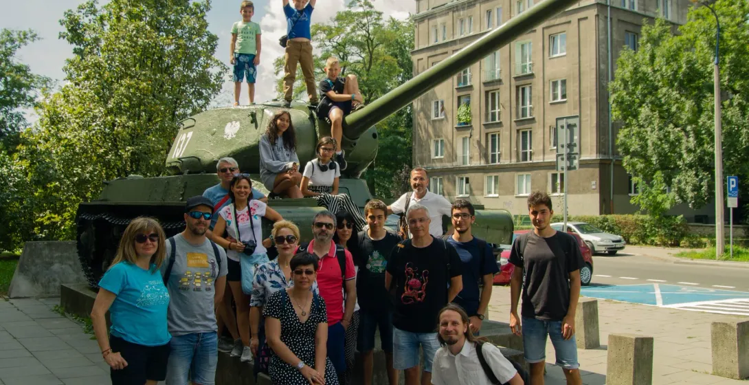 A tour group of adults and children posing for a photo on and around a green IS-2 tank monument in Krakow's Nowa Huta.