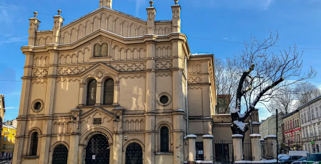 Vista exterior de una gran sinagoga ornamentada con la Estrella de David, cubierta de nieve, bajo un cielo azul en Cracovia.