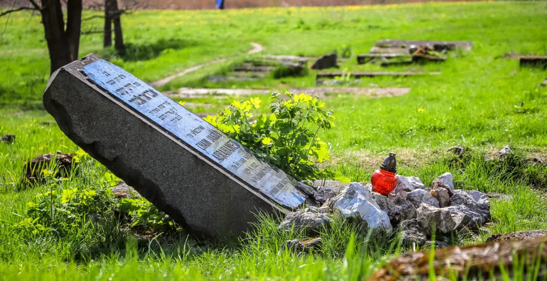 Ein geneigter Grabstein mit einer blauen Tafel und einer roten Grabkerze auf einem grasbewachsenen Feld der Gedenkstätte P...