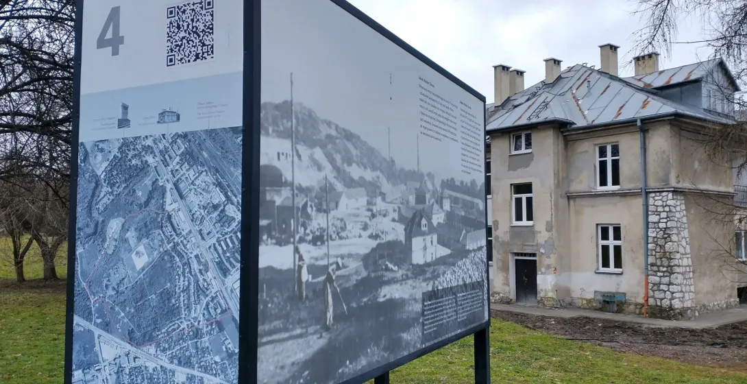 Eine Informationstafel mit Karte und historischen Fotos steht auf einer Wiese vor dem „Grauen Haus“ auf dem Lagergelände P...