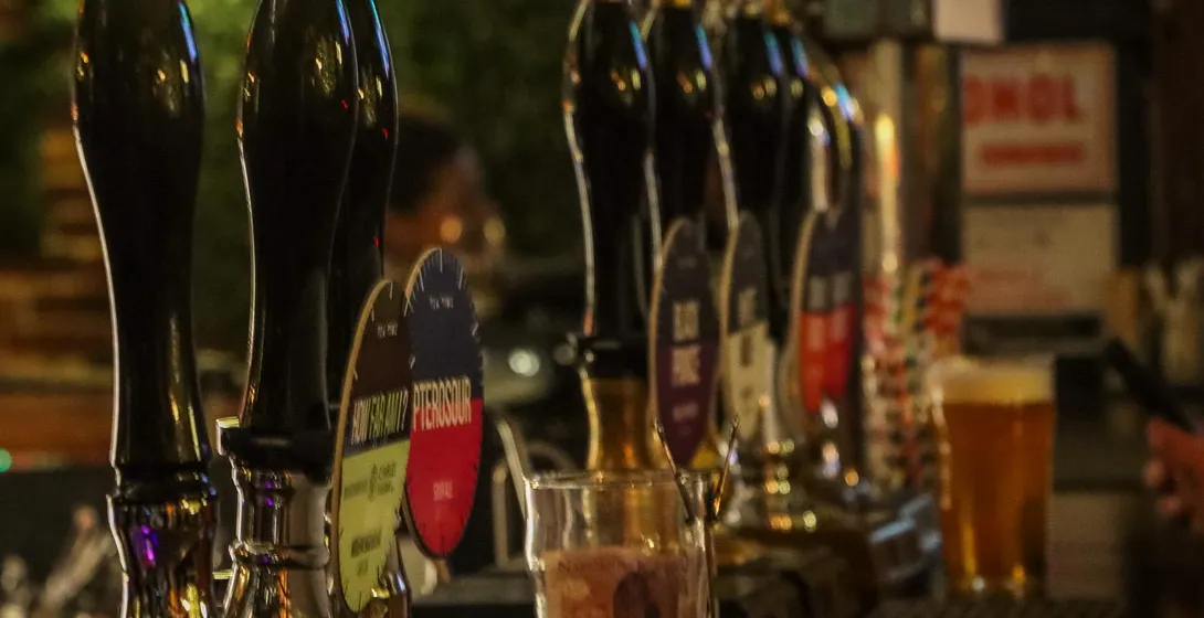 Eine Reihe glänzender schwarzer Zapfhähne auf einer Holztheke in einem schwach beleuchteten Krakauer Pub. Im Hintergrund e...