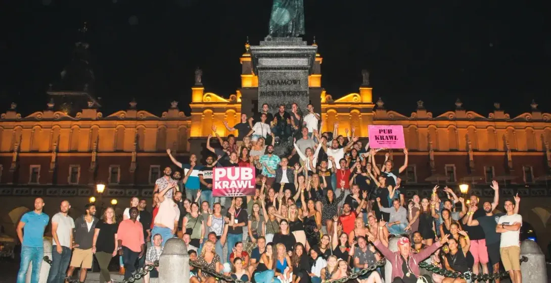 Duża grupa ludzi pozujących nocą przed Pomnikiem Adama Mickiewicza i Sukiennicami na Rynku Głównym w Krakowie.