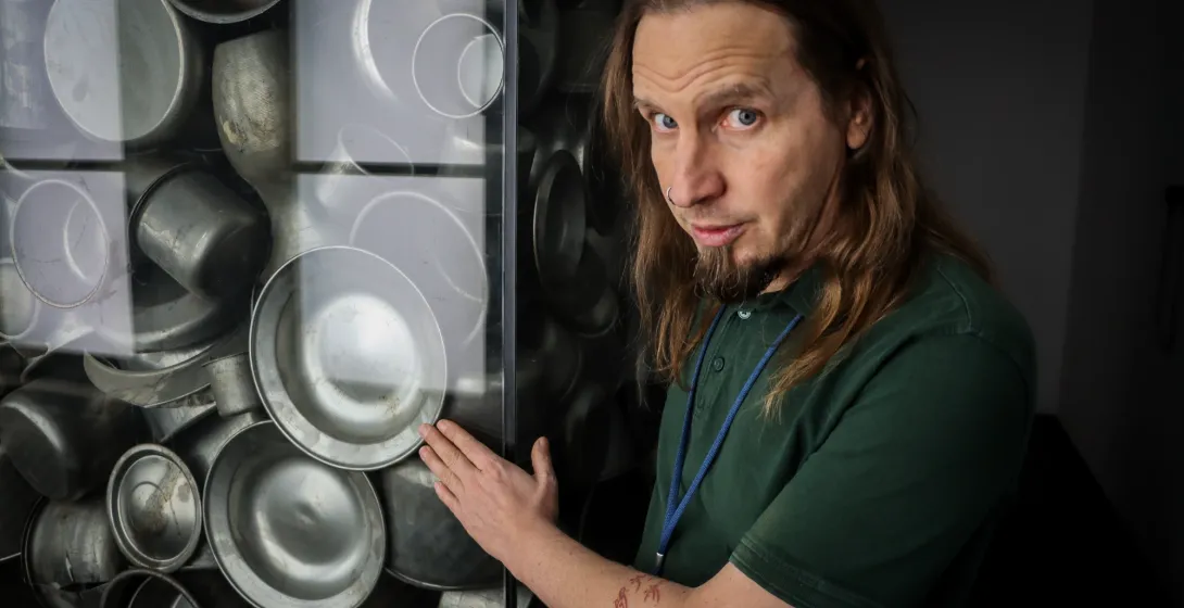 The guide stands beside a glass display filled with reproductions of metal pots like those produced by Schindler's Factory...