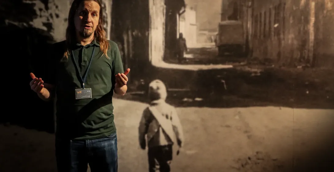 A tour guide gestures while speaking in front of a large historical photograph inside a museum exhibit.
