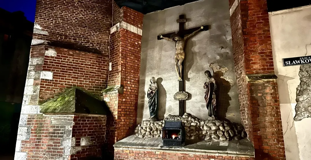 A streetside shrine with a crucifix set into a brick wall on Sławkowska Street in Krakow at night.