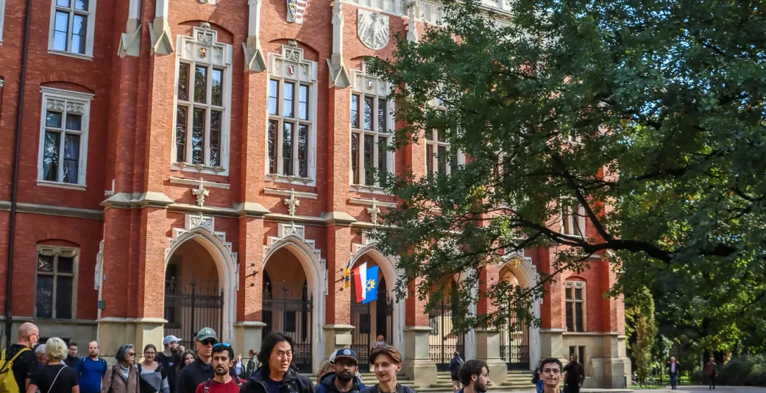 Eine Reisegruppe geht an einem sonnigen Tag an der neugotischen Backsteinfassade des Collegium Novum in Krakau vorbei.