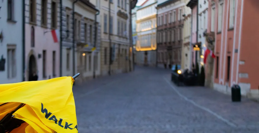 Un paraguas amarillo de Walkative en primer plano, con una vista desenfocada de una calle del casco antiguo de Cracovia.