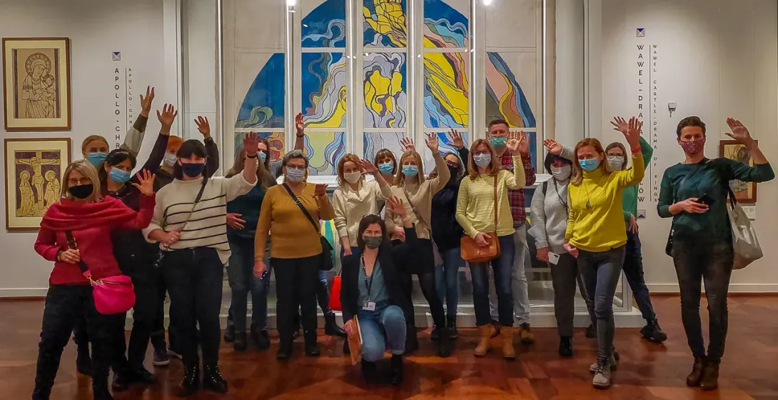 Eine Gruppe von Touristen mit Gesichtsmasken winkt in einem Museum vor einem großen, modernen Kunstwerk.