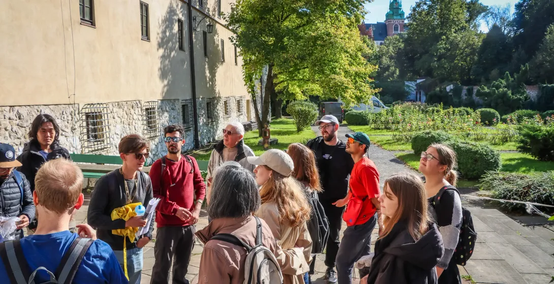 Eine Gruppe von Touristen hört einem Führer auf dem Wawelhügel in Krakau zu, im Hintergrund sind die Domtürme zu sehen.