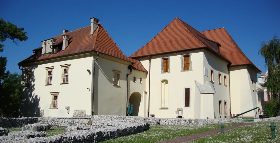 Historic white buildings with red tile roofs at the Wieliczka Salt Mine, with old stone foundations on a lawn in front.