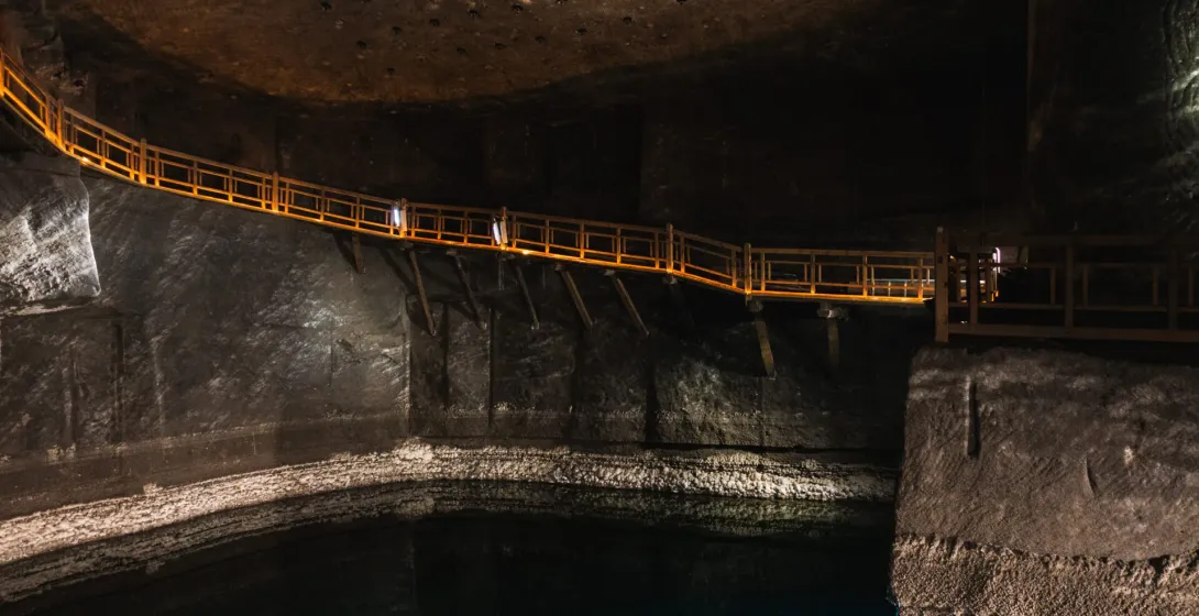 An illuminated wooden walkway runs along the cavern wall above an underground brine lake in the Wieliczka Salt Mine.