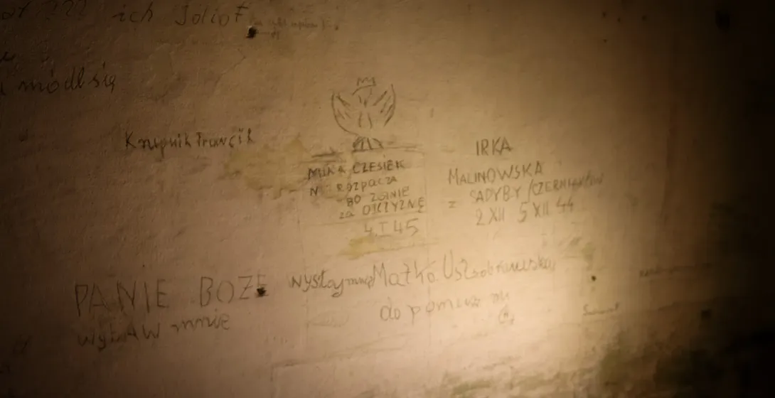 Schwach beleuchtete Wand mit polnischen Inschriften aus dem Zweiten Weltkrieg, darunter ein handgezeichneter polnischer Ad...