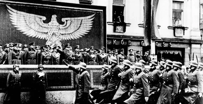 Schwarz-Weiß-Foto einer NS-Militärparade in Krakau. Soldaten marschieren an einer Tribüne mit Offizieren und einem großen ...