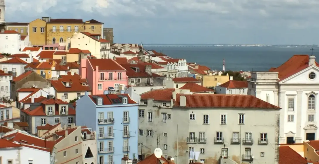 Blick auf das Alfama-Viertel in Lissabon mit roten Dächern, dem Nationalen Pantheon und dem Fluss Tejo.