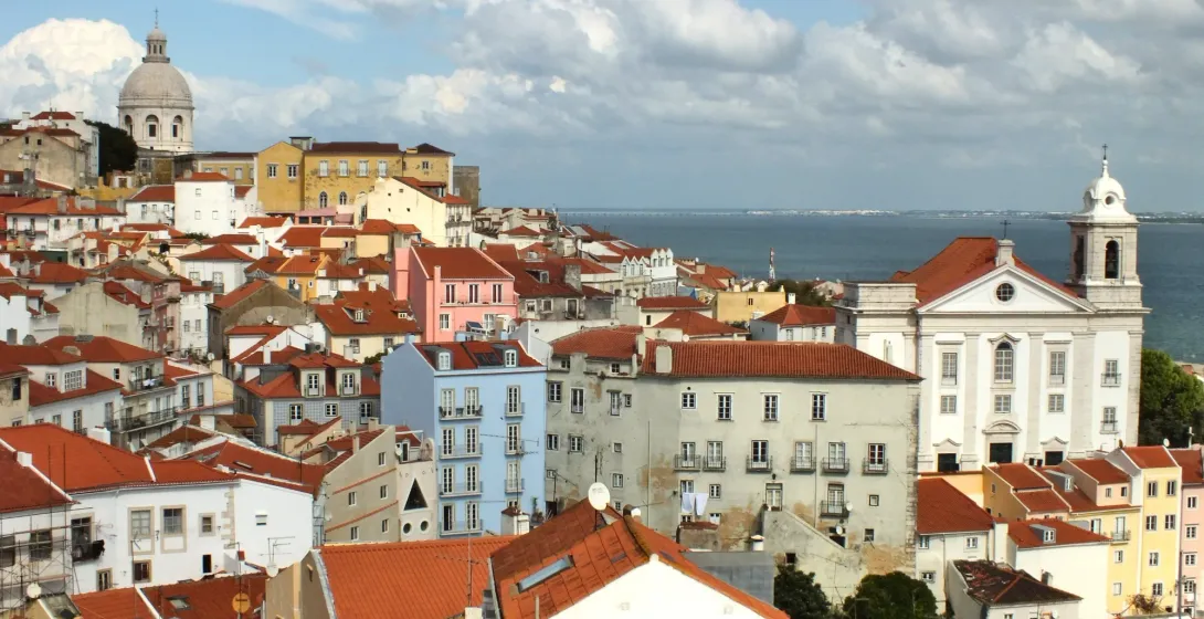 Vista del barrio de Alfama en Lisboa con tejados rojos, el Panteón Nacional y el río Tajo al fondo.