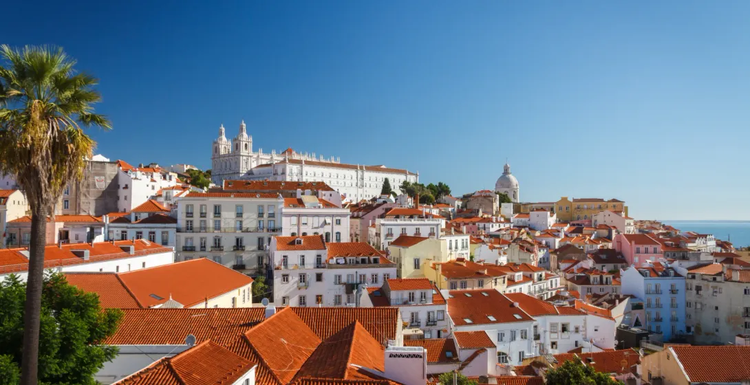 Rote Ziegeldächer im Lissaboner Viertel Alfama mit dem weißen Kloster São Vicente de Fora unter blauem Himmel.