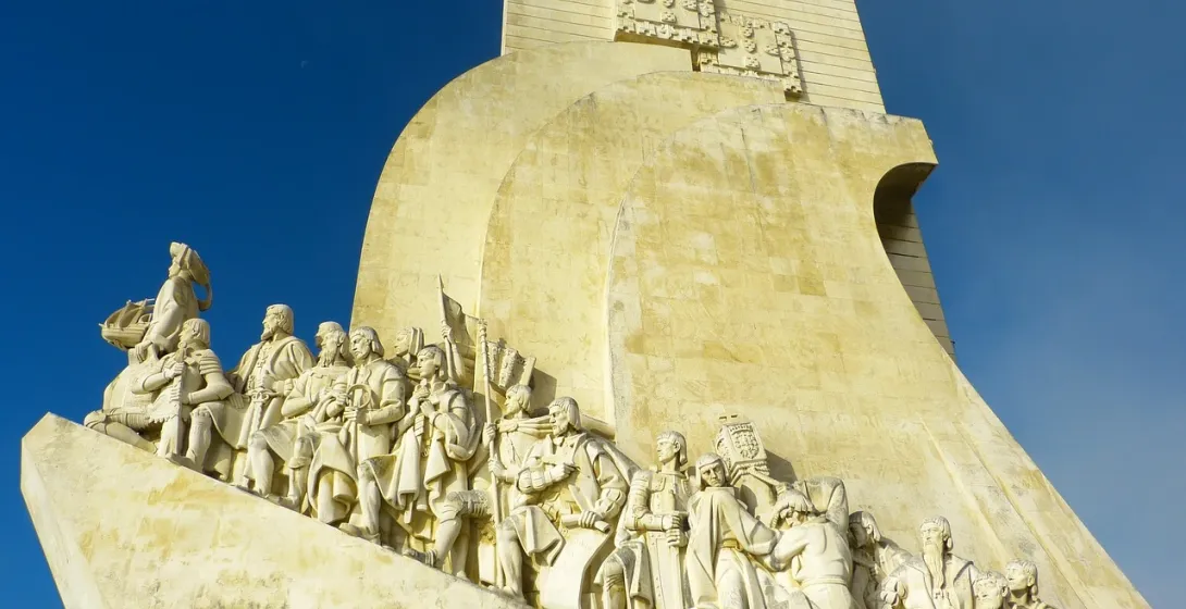 Stone Monument to the Discoveries in Lisbon featuring statues of historical explorers on a ship's prow against a blue sky.