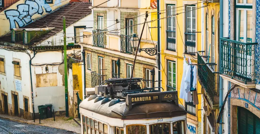 Yellow Tram 28 climbing a steep, cobbled street lined with traditional tiled buildings in Lisbon.