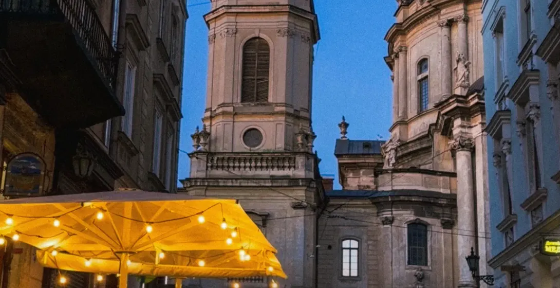Ein belebtes Straßencafé in Lemberg bei Dämmerung, mit der Dominikanerkirche im Hintergrund unter einem tiefblauen Himmel.