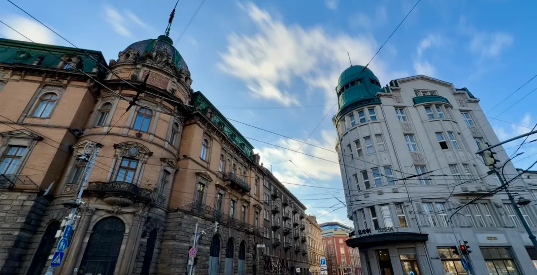 Weitwinkelaufnahme von zwei historischen Gebäuden an einer nassen Kopfsteinpflasterstraße in Lemberg unter blauem Himmel.