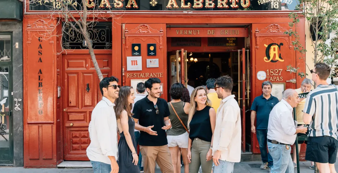 Un guía turístico habla con los turistas frente a la fachada roja de la histórica taberna Casa Alberto de Madrid.