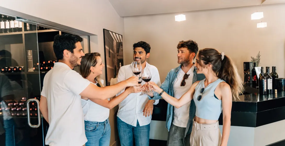 Un grupo de cinco jóvenes brindando con copas de vino tinto en una vinoteca moderna.