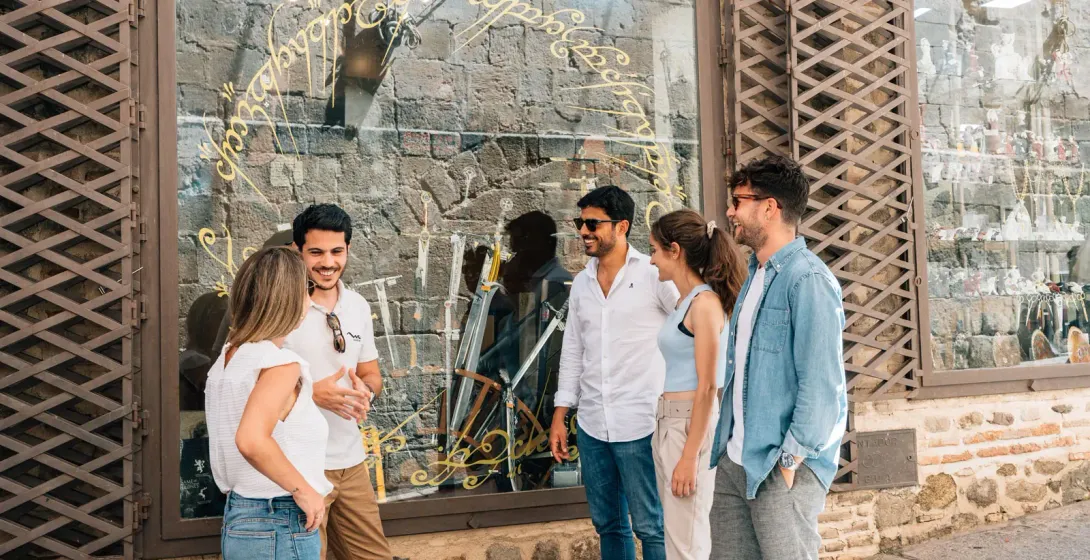 Un grupo de cinco jóvenes conversando frente a una tienda con una inscripción dorada en el escaparate.