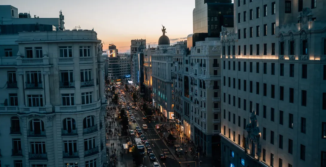 Vista elevada de la concurrida calle Gran Vía de Madrid al atardecer, con coches y peatones en las aceras.