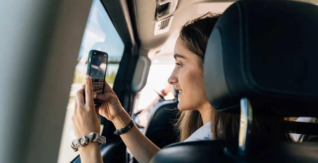Una joven sentada en el asiento trasero de un coche hace una foto del paisaje con su smartphone.