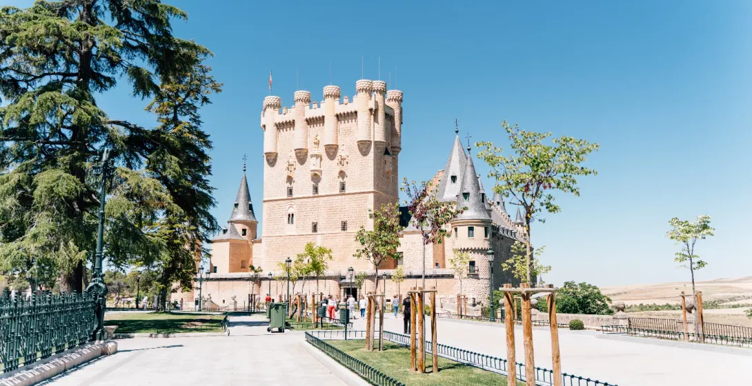 El Alcázar de Segovia, un castillo de piedra con torretas, visto desde un parque en un día soleado.