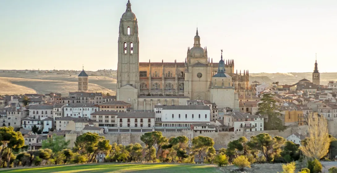 La Catedral de Segovia sobre el casco antiguo, vista desde una colina verde al atardecer.