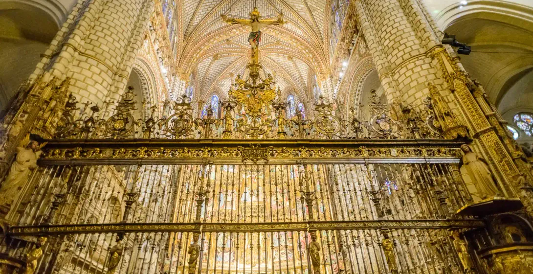 Reja dorada ornamentada bajo un crucifijo y un alto techo abovedado en el interior de la Catedral de Toledo, España.