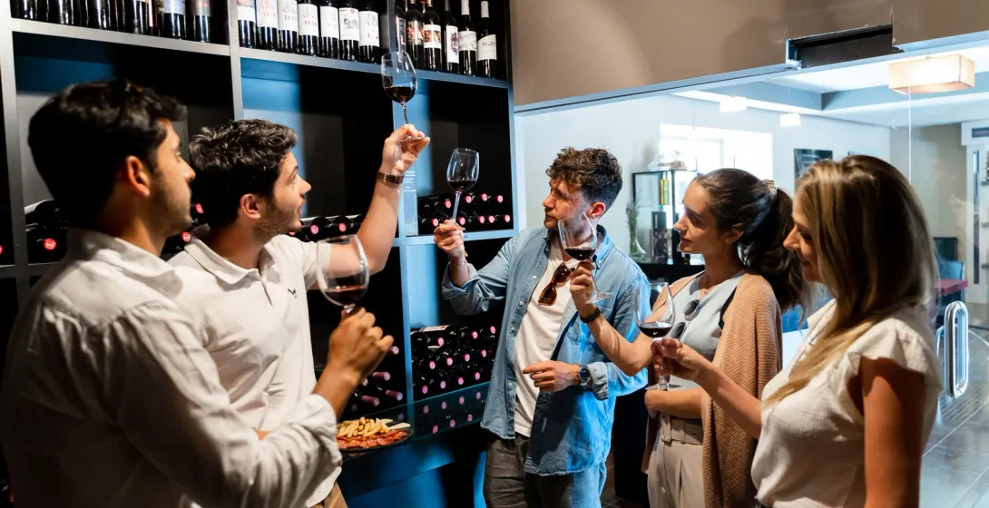 Un grupo de personas catando vino tinto en una tienda. Un hombre levanta su copa para inspeccionar el color del vino.