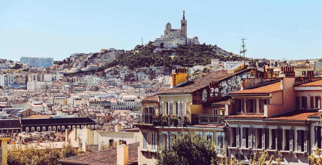 Panoramic view of Marseille with Notre-Dame de la Garde basilica on a hill, surrounded by dense urban buildings with red r...