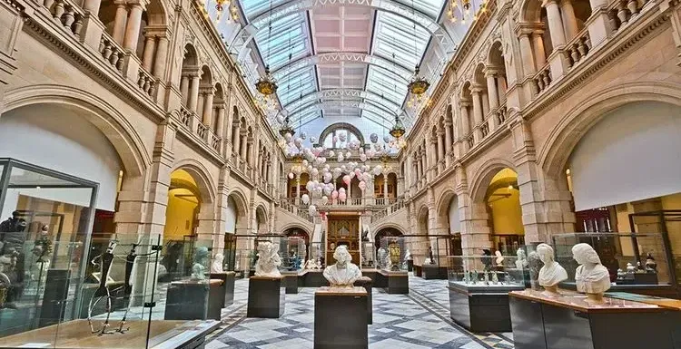 Interior of the Kelvingrove Art Gallery and Museum in Glasgow, with stone pillars, a glass roof, and sculpture exhibits.