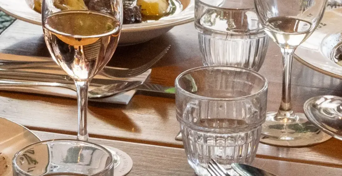 Table set with plates of stew, wine glasses with rosé, and water glasses in a restaurant setting. Focus on food.