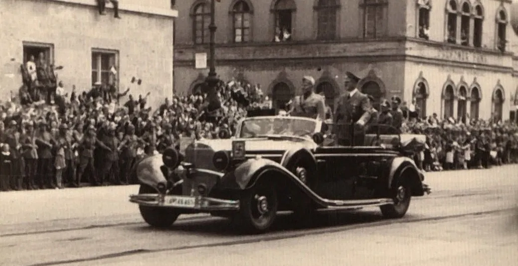 Historical photo of Adolf Hitler in an open car passing crowds giving the Nazi salute in Munich.