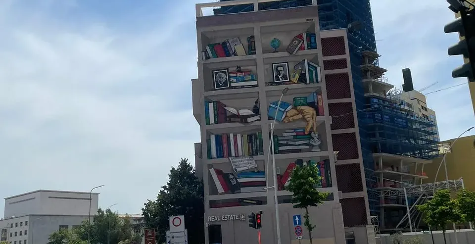 Scena uliczna z budynkiem z dużym muralem przedstawiającym półki z książkami.
