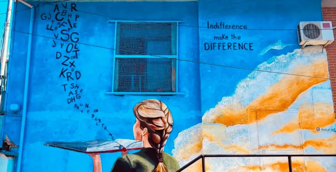 Kolorowy mural przedstawiający kobietę z książką na niebieskim budynku.