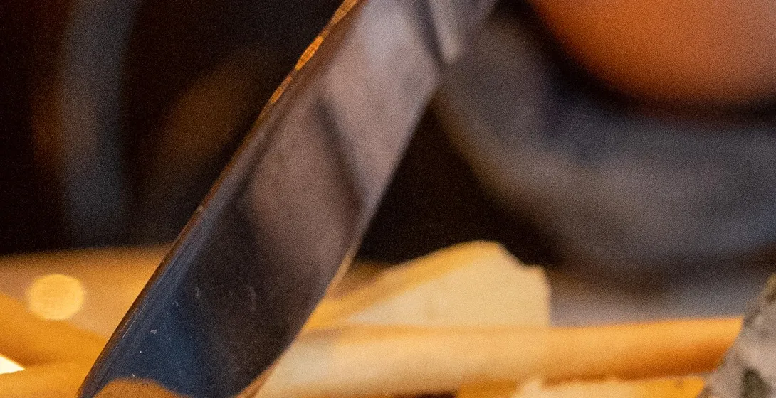 Primer plano de una mano con esmalte rojo cortando un trozo de queso de corteza blanca en un plato con palitos de pan.