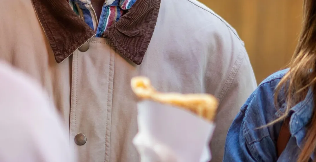 Hombre sonriente observando cómo se entrega un crêpe a una persona con chaqueta vaquera en la calle.