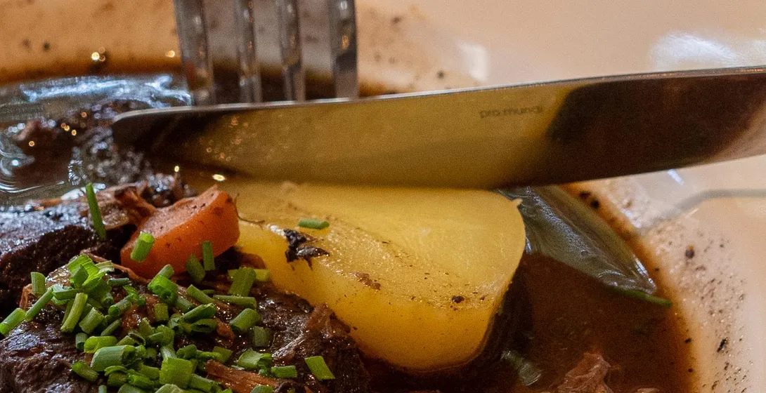 Close-up of a rustic dish, possibly Coq au Vin or beef bourguignon, with a fork. Rich stew, potato, chives.